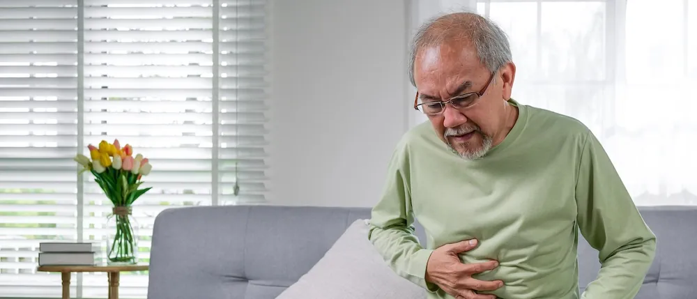 Older man in pain holding his abdomen on a couch, a common sign of Covidien hernia mesh complications