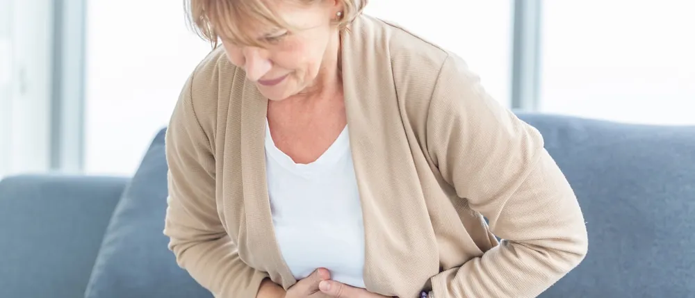 Woman holding her abdomen in pain on a couch, a possible sign of Symbotex hernia mesh complications
